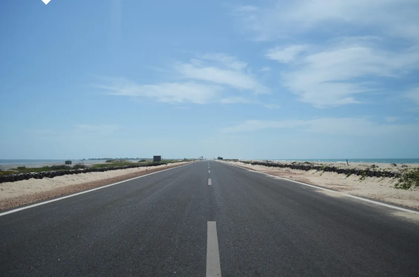 Straight tarmac road leading towards Dhanushkoti with sea visible on both sides under a clear blue sky in Tamil Nadu.