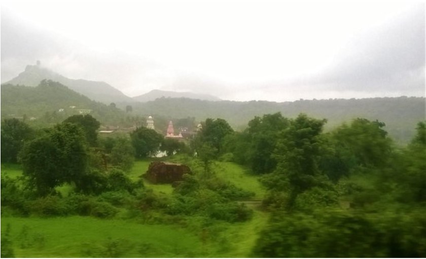 A serene travel story captured through a train window, showing lush green fields, scattered trees, distant hills, and a small village temple complex nestled in the landscape under a misty sky.