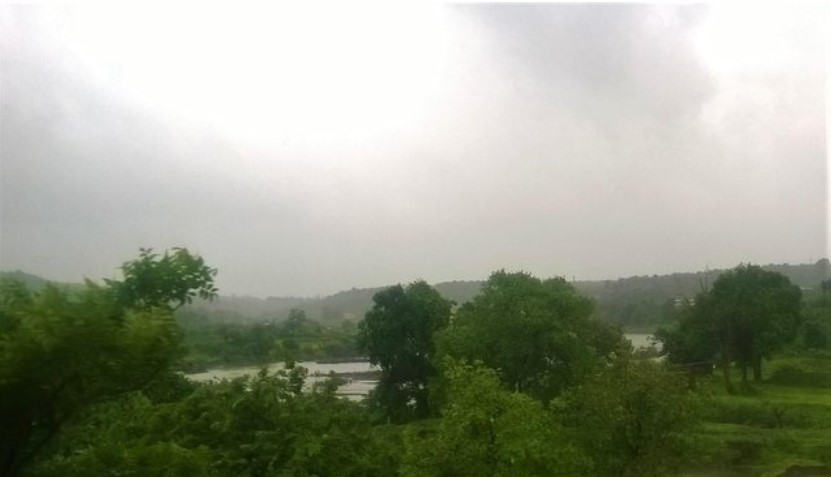 A peaceful travel story captured through a train window, showing mist-covered hills, lush green trees, and a river winding quietly through the landscape under a cloudy sky