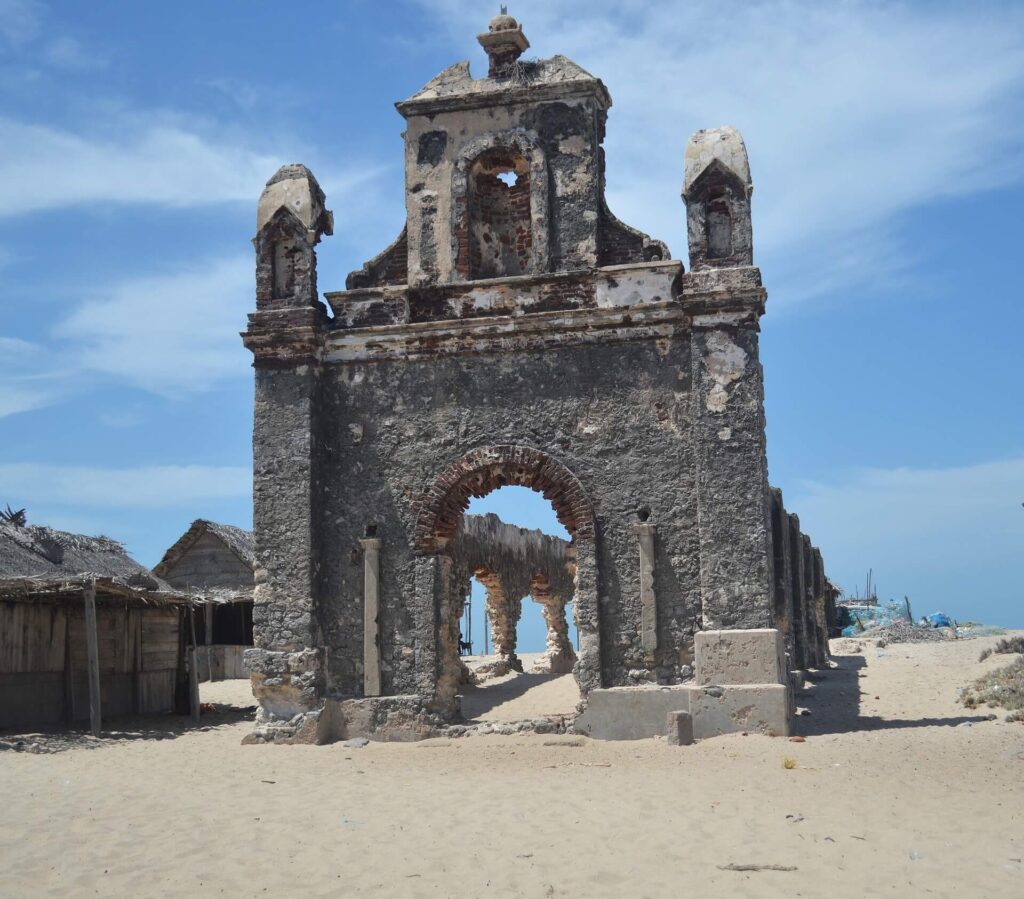 Ruined church structure at Dhanushkoti ghost town in Tamil Nadu, with arched stone walls and sea visible in the background.