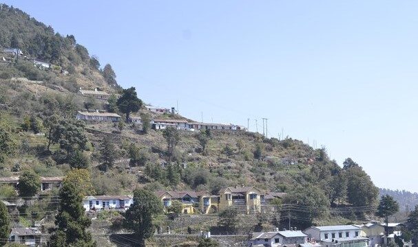 A hillside view in Nainital with colorful houses scattered among trees under a clear blue sky.