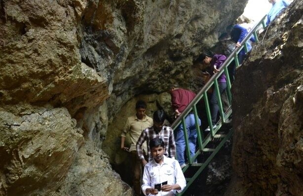 Visitors carefully climb narrow stairs inside a rocky cave formation in Nainital, surrounded by rugged stone walls