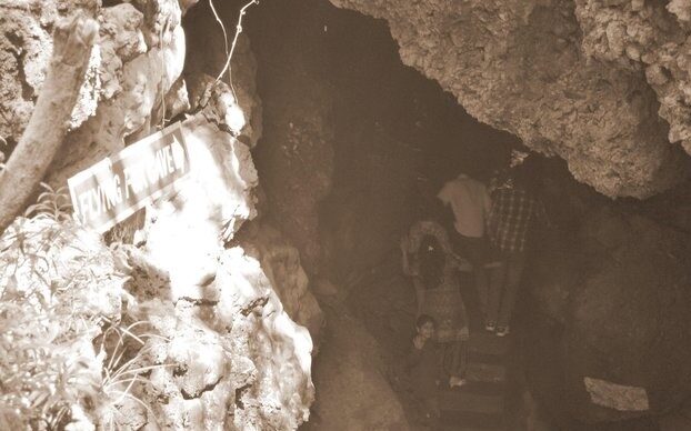 A group of visitors enters a dimly lit rocky cave passage in Nainital, with a sign reading “Flying Fox Cave” visible near the entrance