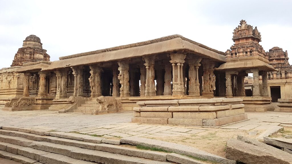 Ancient stone temple at Hampi with carved pillars, ornate towers, and stone steps leading up to the mandapa.