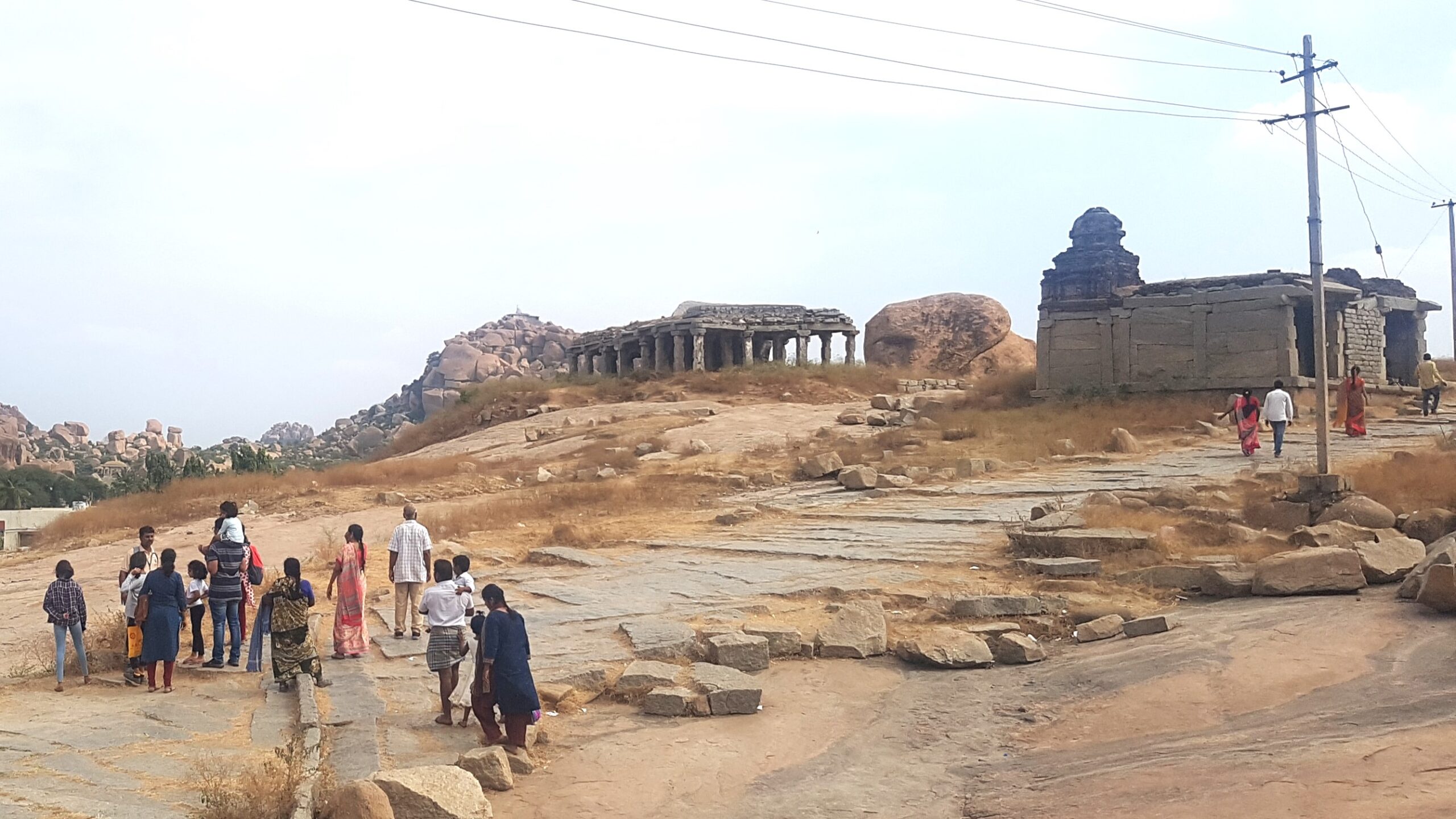Tourists walking among ancient stone structures and rocky terrain at Hampi, Karnataka