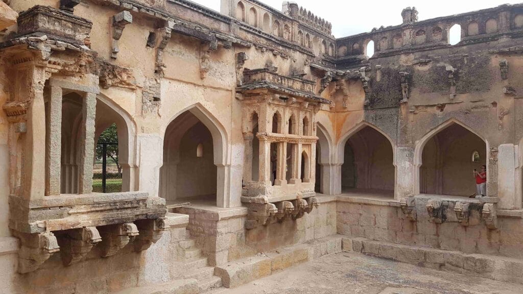 Interior view of the Lotus Mahal area in Hampi, featuring arched entrances, Indo-Islamic architectural details, and weathered stone balconies with intricate carvings.