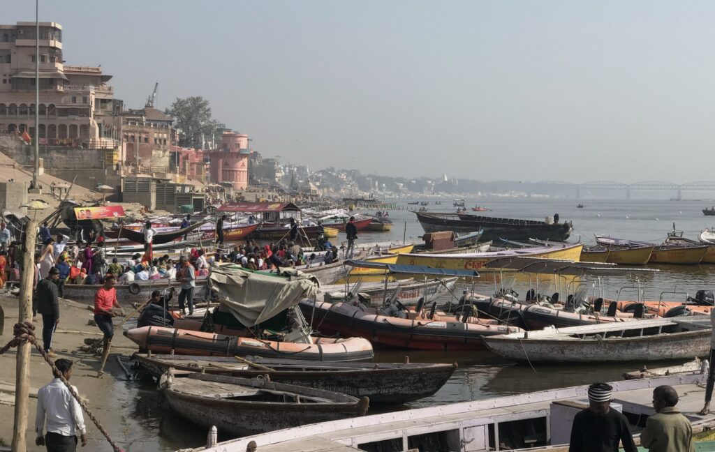 A busy morning at the ghats of Varanasi with colorful boats anchored along the River Ganga and devotees gathering on the banks for rituals and rides.
