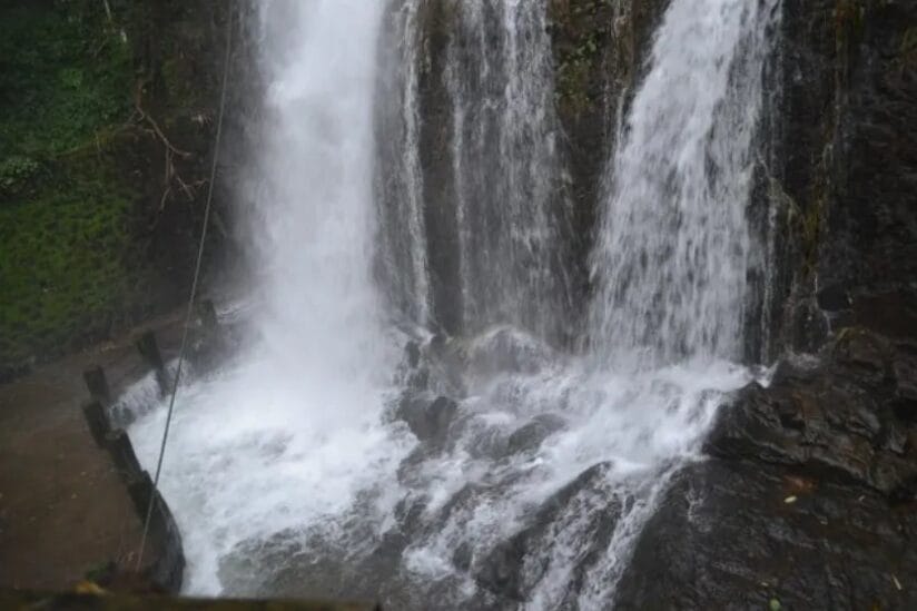 Close view of a strong waterfall cascading over dark rocks in a lush forest during monsoon.