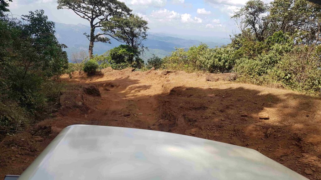 A rough, uneven uphill jeep track with deep ruts leading toward an open valley view on the Kudajadri climb.
