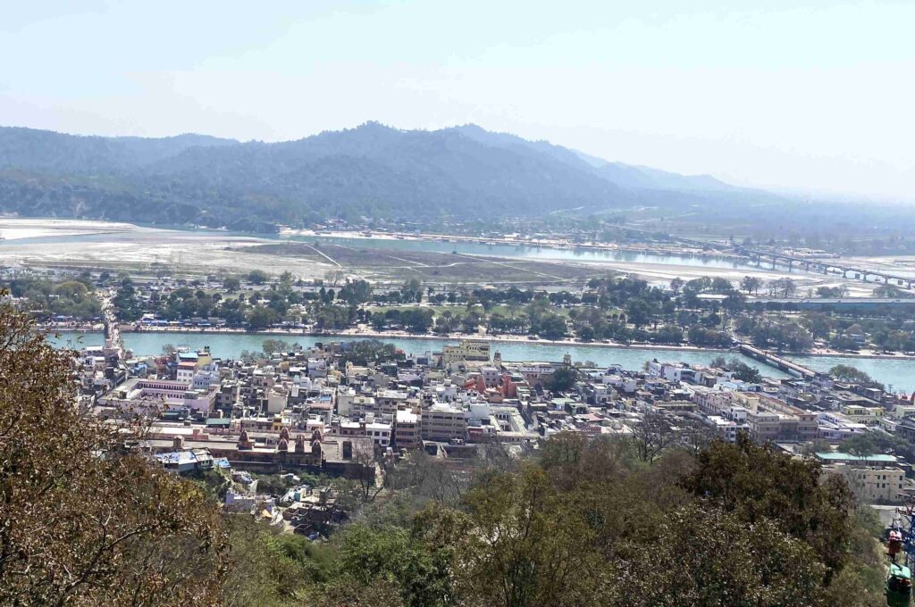 A panoramic view of Haridwar from the cable car, showing the Ganga river winding through the city with hills in the background.