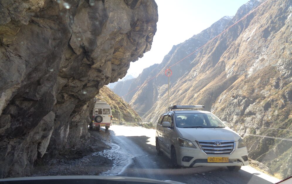 Narrow mountain road running along a steep rocky cliff with deep valleys below, captured on the Badrinath route.