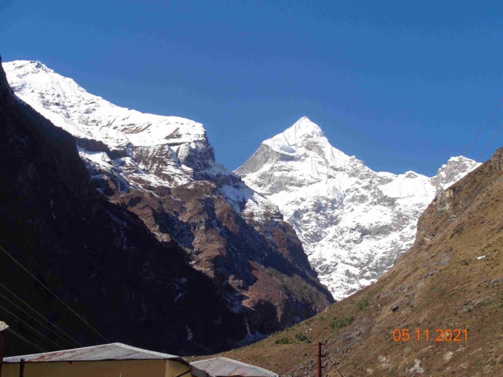 Snow-covered Himalayan mountains with a sharp white peak rising between two dark valley walls on a clear sunny day.