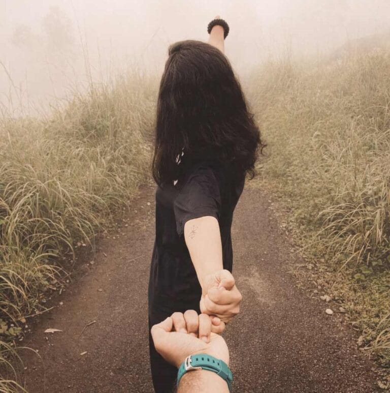 Person holding another’s hand while walking along a misty path, symbolizing hope, guidance, and moving forward together.”