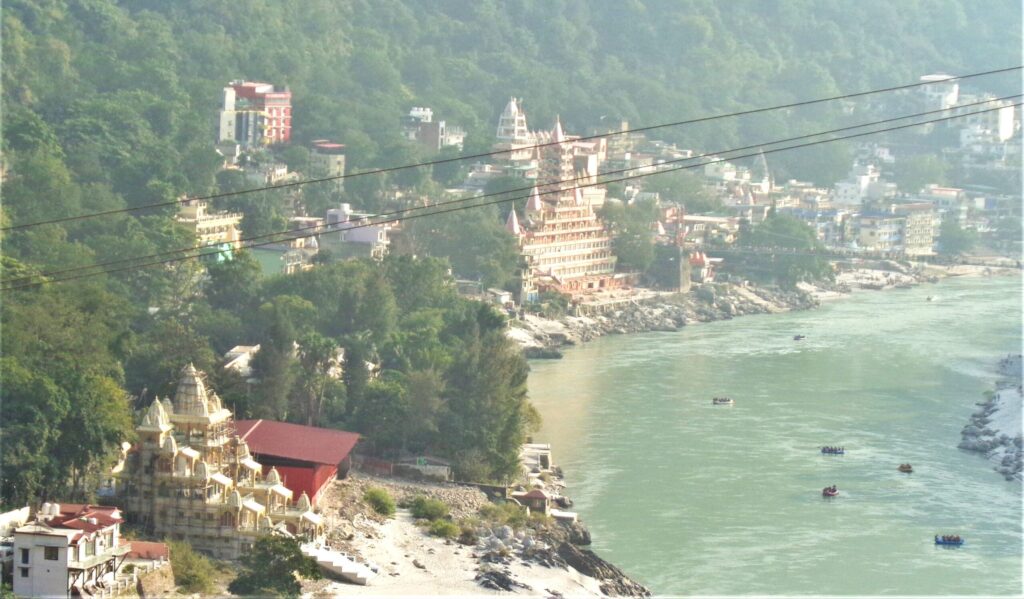 Rafting boats floating on River Ganga with Rishikesh town along the riverbank