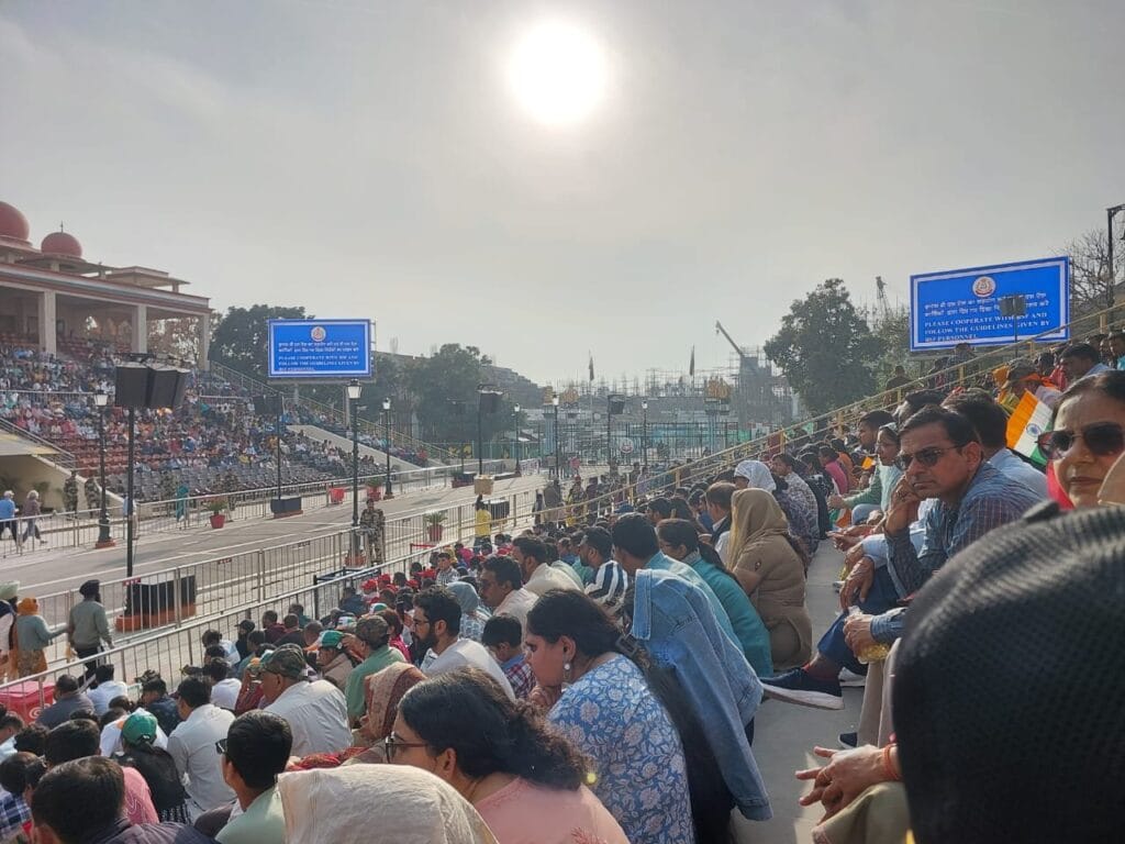 Spectators seated in the gallery under the afternoon sun at Wagah Border, waiting for the Beating Retreat ceremony, with parade grounds and border gates visible ahead.