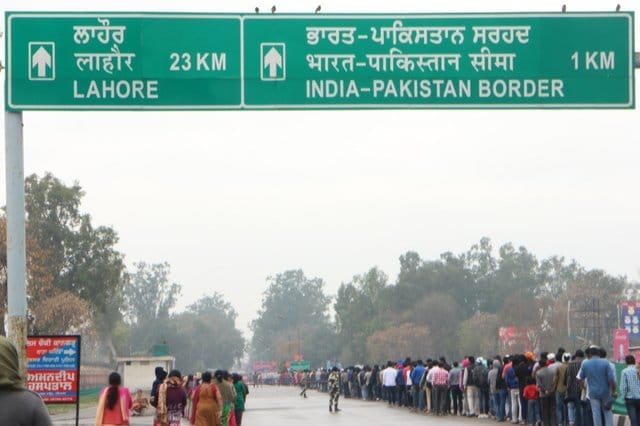 Visitors walking towards Wagah Border under Lahore and India–Pakistan Border road sign near Amritsar